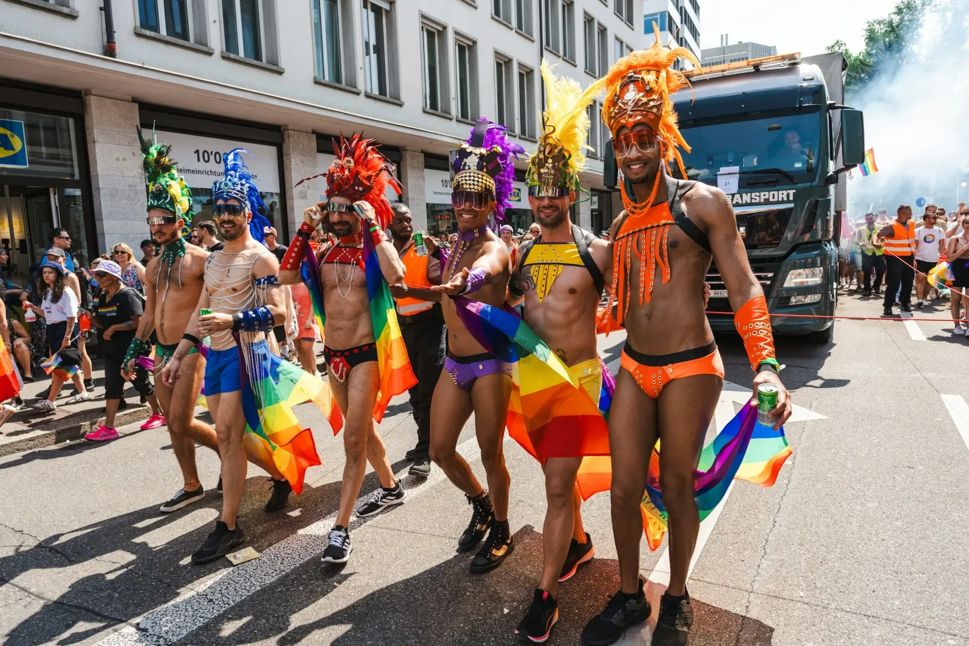 Groupe d'hommes en costumes Pride colorés avec coiffes à plumes et drapeaux arc-en-ciel lors d'une manifestation Pride à Zurich.
