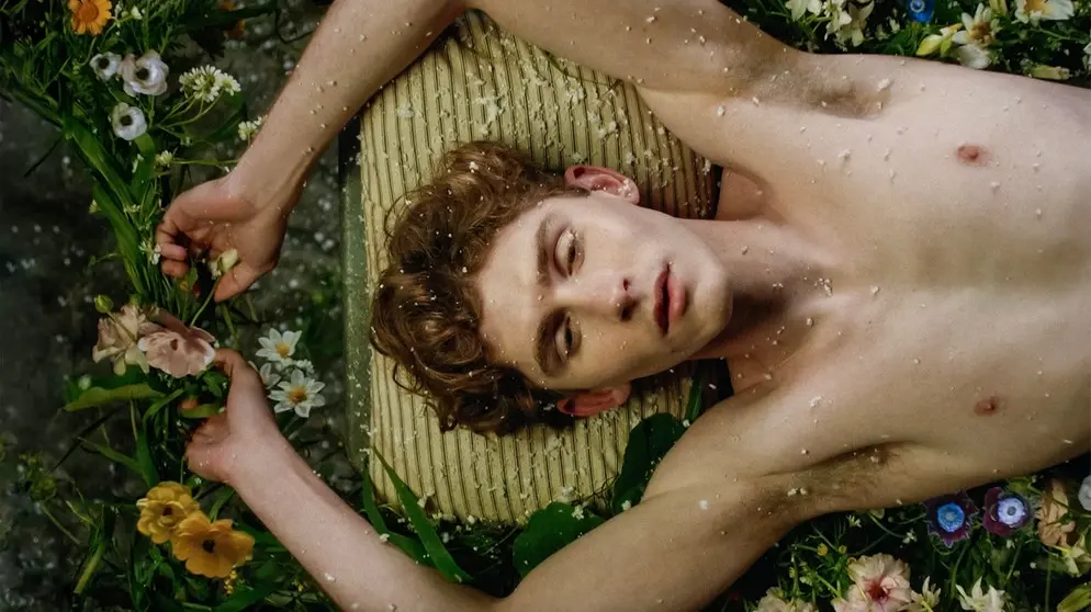 Junger Mann liegt oberkörperfrei auf einer Matratze, umgeben von bunten Blumen – Szene aus dem Film «Lilies Not for Me» (2024).