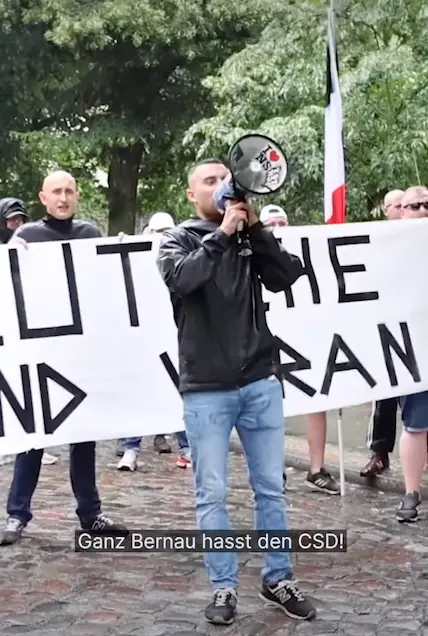 Un homme qui manifeste tient un mégaphone à la main et crie « Tout Bernau déteste la CSD ! »