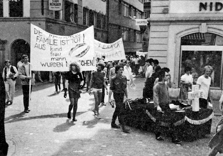 Des manifestant·e·s tiennent une pancarte portant l'inscription «Die Institution Familie ist Tot! Aus KIND, FRAU, MANN wurden Menschen!» (L'institution de la famille est morte ! De l'ENFANT, de la FEMME, de l'HOMME sont devenus des êtres humains !)