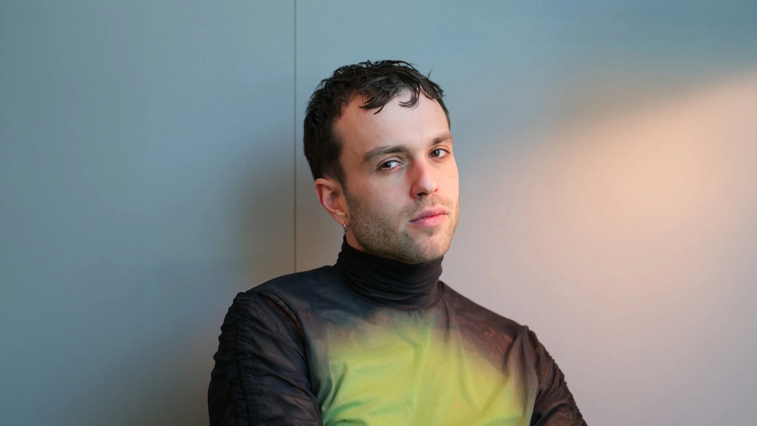 Porträt von Andri Oppliger, Gründer der genderneutralen Modemarke ANOP, vor blauem Hintergrund.