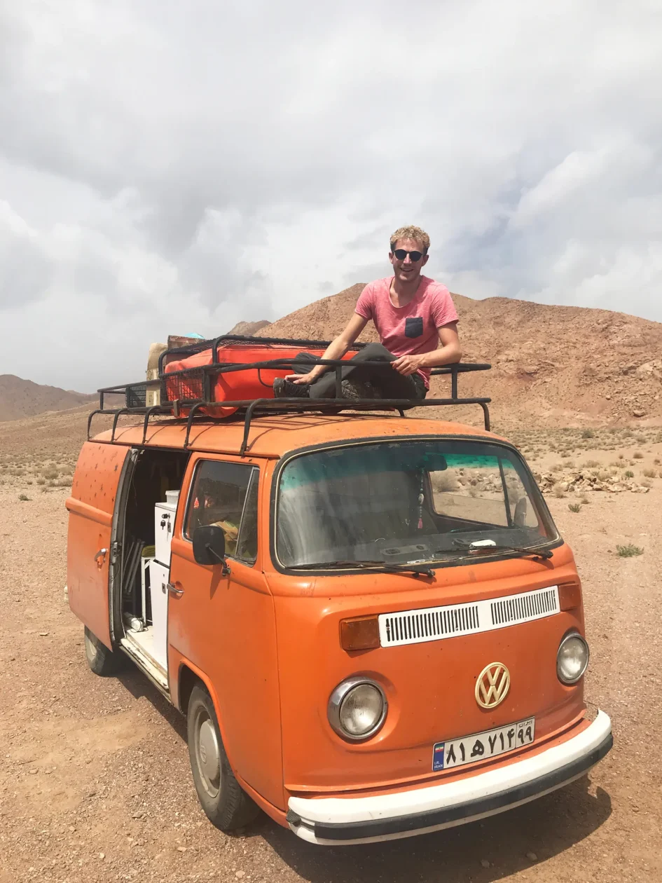 Michael Elsener assis sur un break orange dans le désert iranien