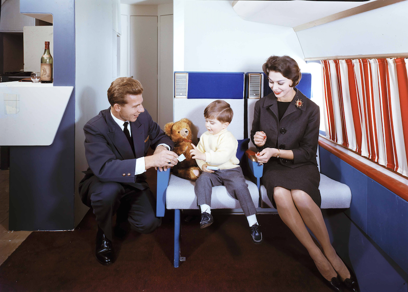 Mama und Papa in einem Flugzeug, ihr Kind sitzt zwischen ihnen.