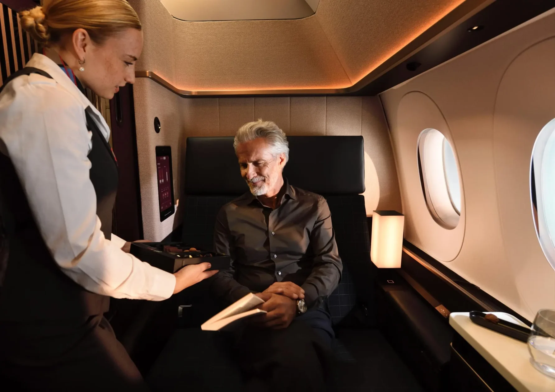 Ein Mann, der in einem Sitz der ersten Klasse sitzt, wird von einer Flugbegleiterin bedient.