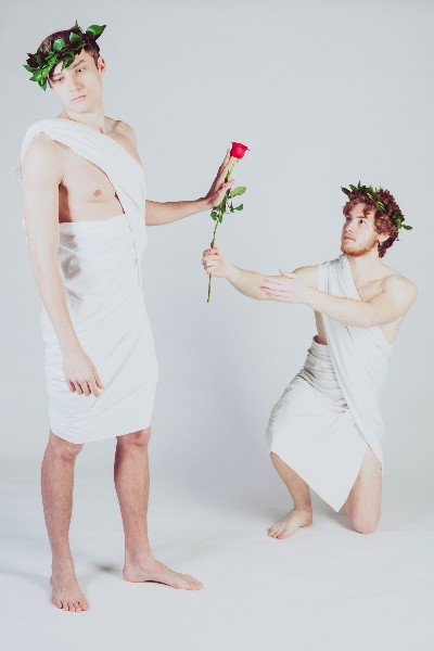 Zwei Männer in weissen Togas mit Blätterkranz, einer reicht dem anderen eine Rose