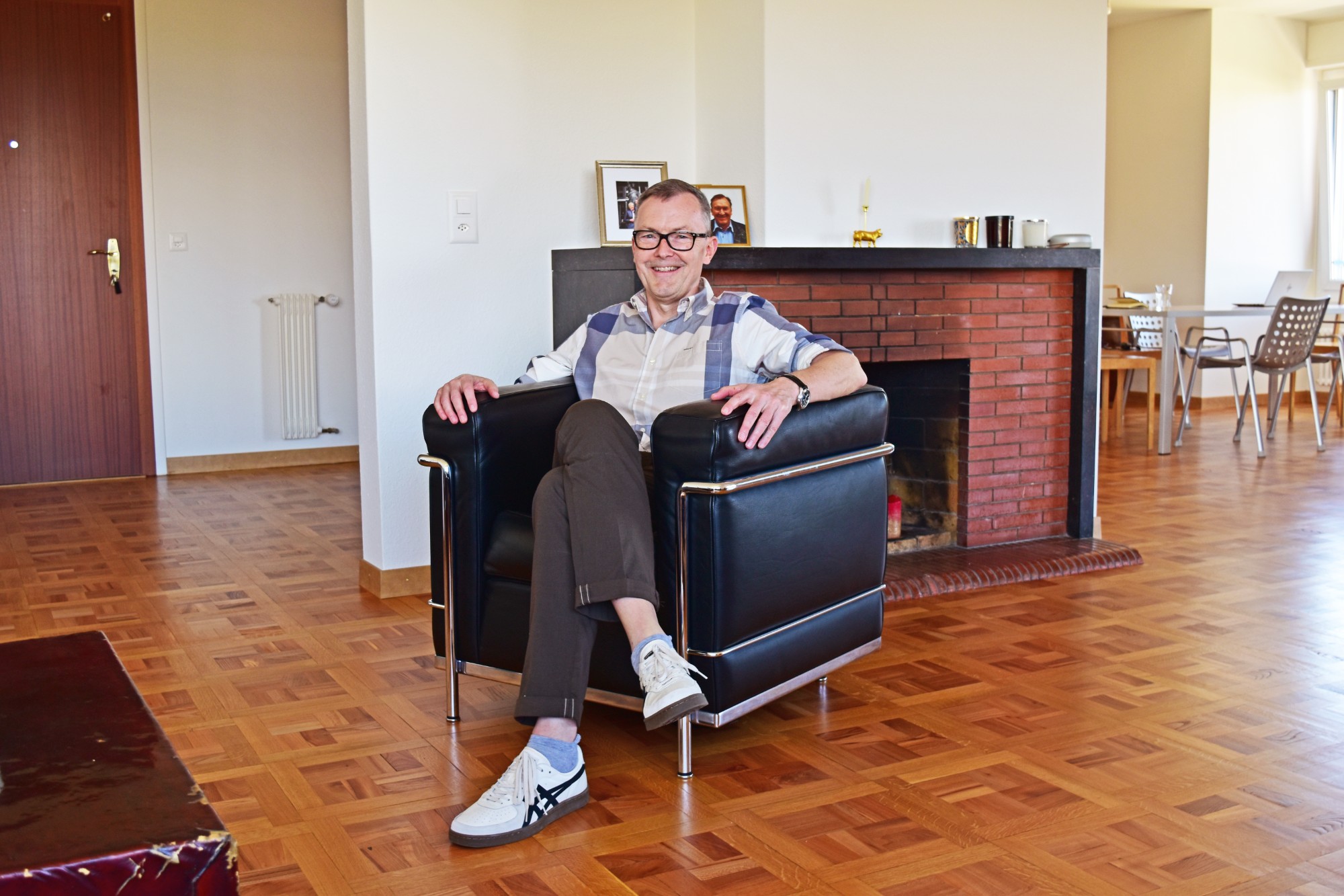 Jürg Lauber sitzt mit überschlagenen Beinen in einem schwarzen Ledersessel vor einem Backsteinkamin