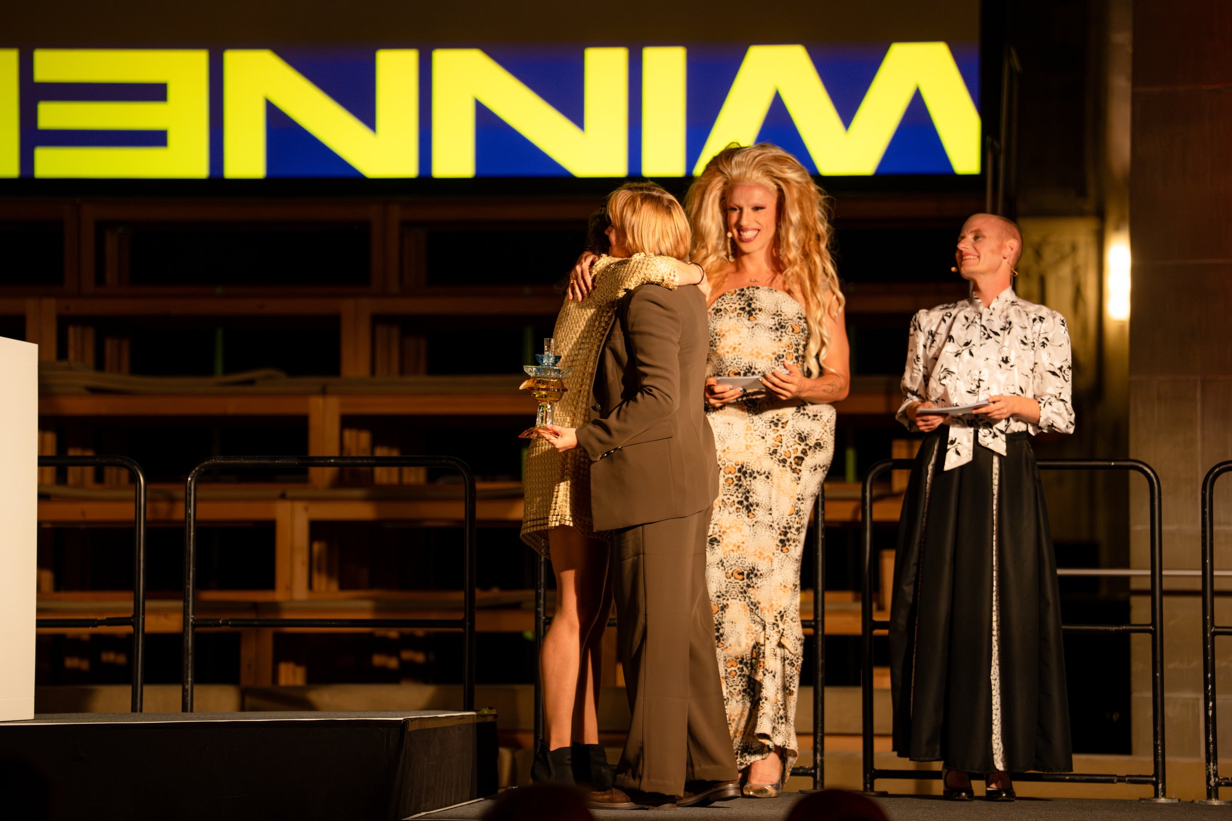 Umarmung auf der Bühne vor einer gelben Winner-Leinwand