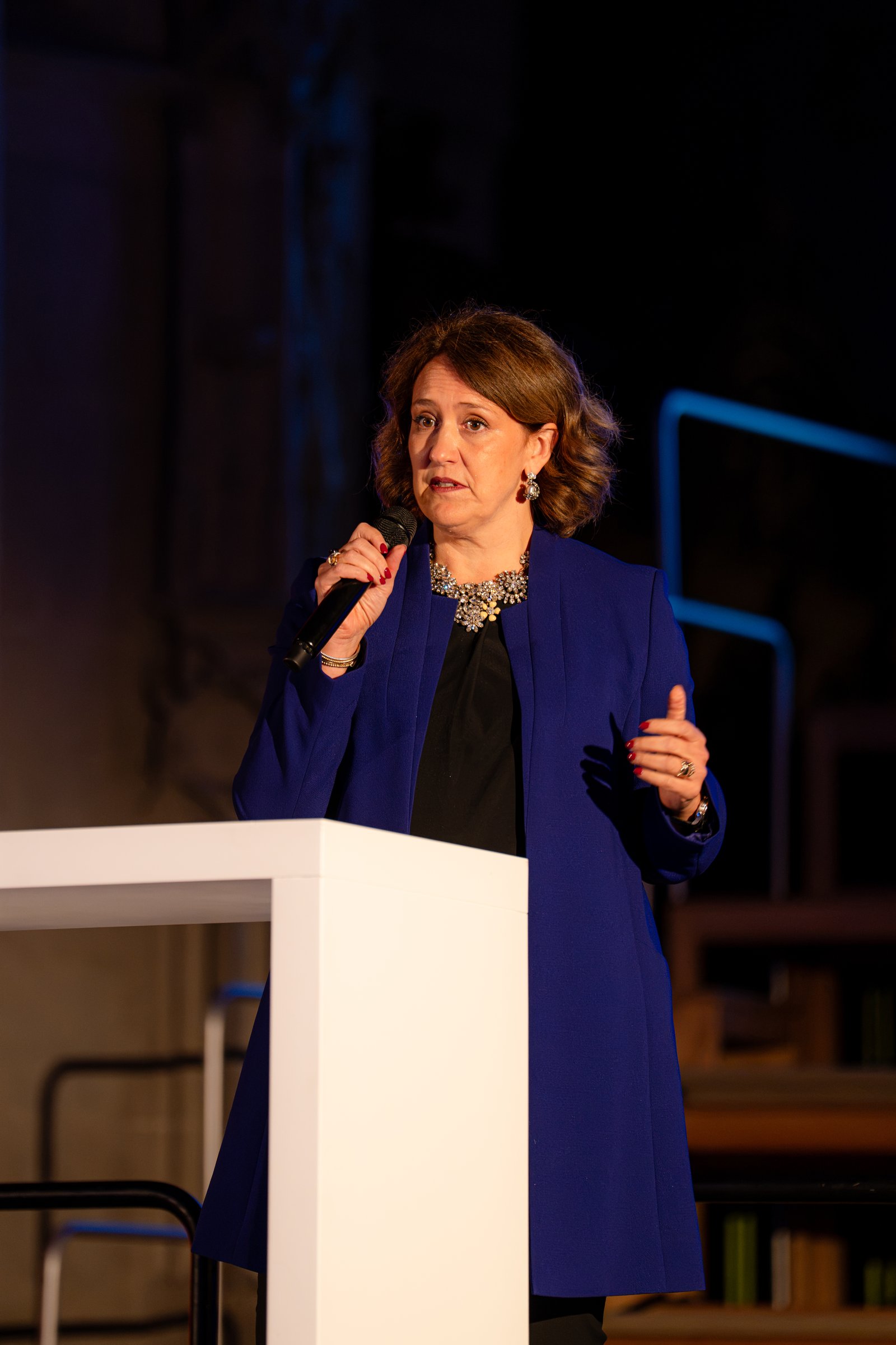 Eine Rednerin im blauen Blazer spricht am weissen Pult ins Mikrofon